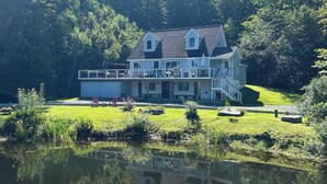A two-story house with a balcony, surrounded by a pond and lush greenery. - Beaver's Bend Lakefront Retreat ~16 mi to Slopes & Pet Friendly! (Whitingham)