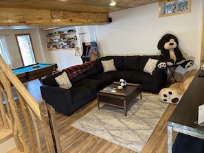 A cozy living room with a sectional sofa, a pool table, and a large stuffed dog.