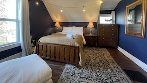 Un dormitorio con cama, mesitas de noche, cómoda, espejo y ventana con cortinas.