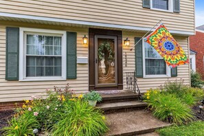 A house with a front door, green shutters, and a colorful flag. - The Henry House I Pet Friendly, Cozy, Convenient (Fairview Park)