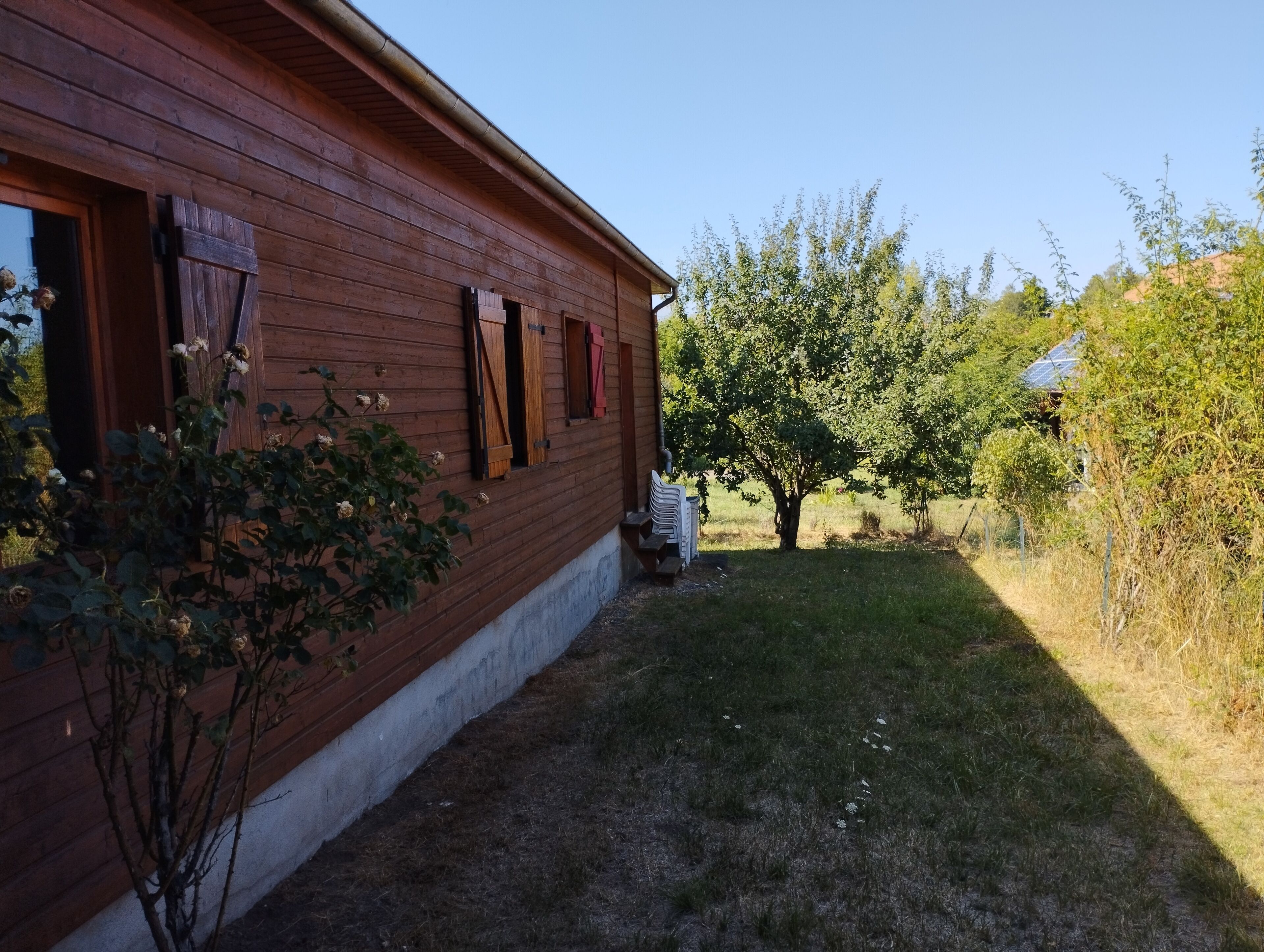 Une maison en bois avec un toit en pente, un petit jardin avec un arbre et un ciel dégagé.