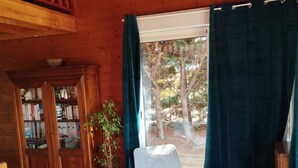 A cozy living room with a wooden ceiling, a bookshelf, a potted plant, two chairs, a coffee table, and a large window with curtains. - Chalet Les Adrets de Sancy-au Coeur de L'auvergne (Saint-Diéry)