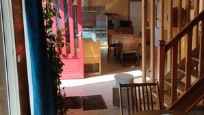A cozy living area with a wooden staircase, a dining table, and a kitchen in the background. - Chalet Les Adrets de Sancy-au Coeur de L'auvergne (Saint-Diéry)