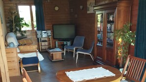 A wooden cabin interior with a dining table, chairs, a television, and a bookshelf. - Chalet Les Adrets de Sancy-au Coeur de L'auvergne (Saint-Diéry)