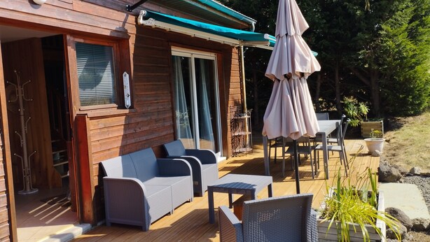 A wooden deck with outdoor furniture, a covered patio area, and a view of the surrounding landscape. - Chalet Les Adrets de Sancy-au Coeur de L'auvergne (Saint-Diéry)