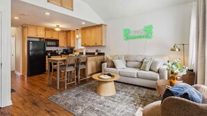 A modern kitchen with wooden cabinets and a black refrigerator, a dining area with a round table, and a living room with a sofa and a coffee table. - Newly Renovated Tremont Treasure I Cozy + Modern (Cleveland)