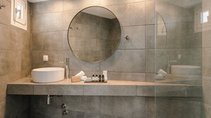 Un bagno moderno con uno specchio rotondo, un lavandino e una cabina doccia in vetro.
