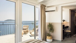 Una camera d'albergo con balcone, un letto, una pianta in vaso, una scrivania e una sedia.