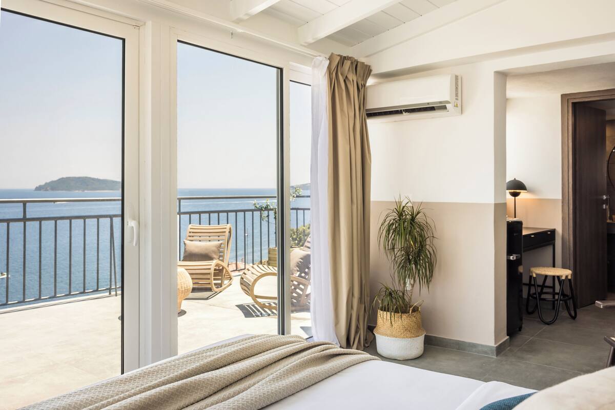 A hotel room with a balcony, a bed, a potted plant, a desk, and a chair.