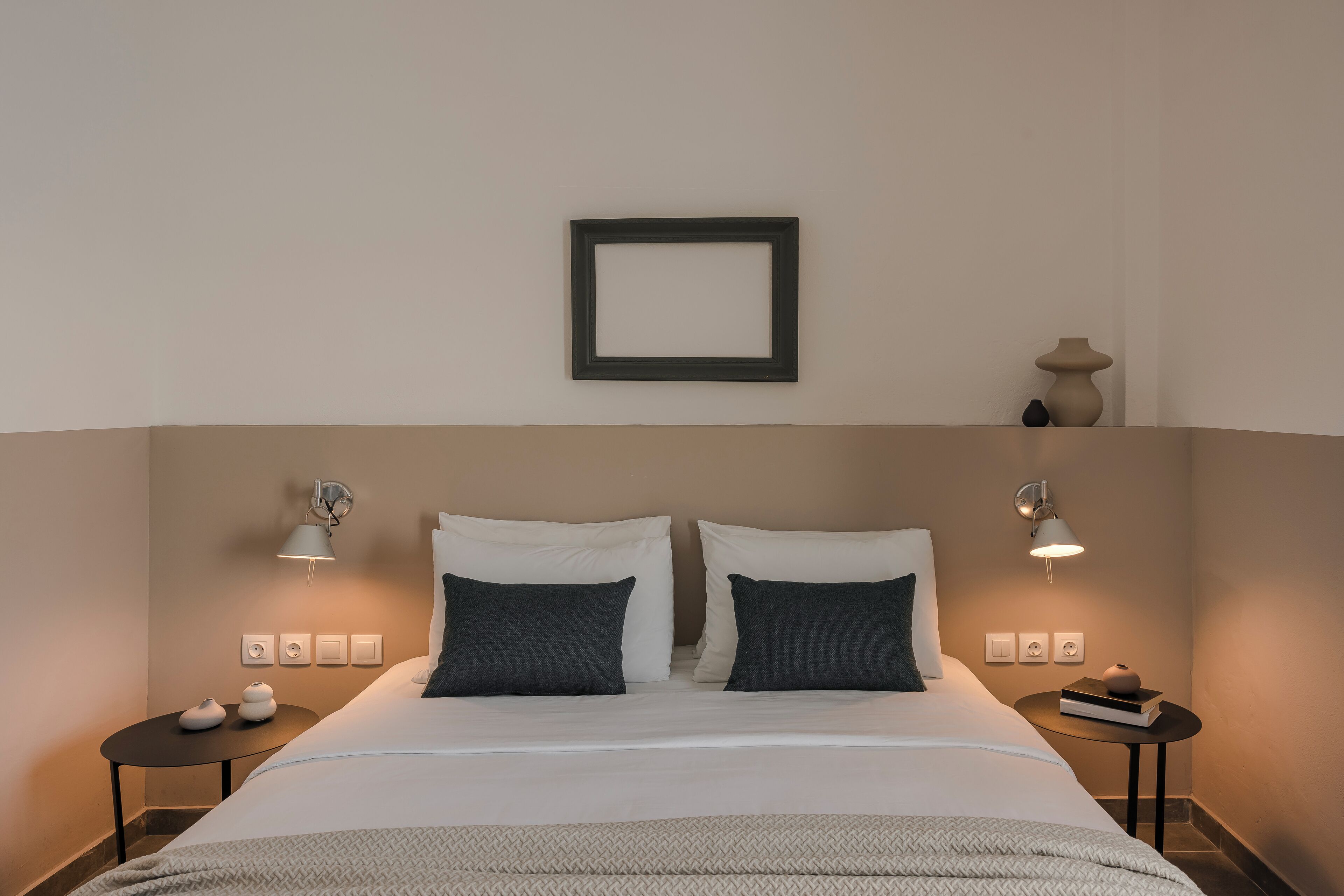Ein ordentlich eingerichtetes Hotelzimmer mit einem Bett, zwei Nachttischen und Wandleuchten.