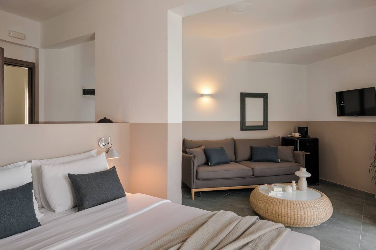 A modern hotel room with a bed, a sofa, a round coffee table, and a flat-screen TV.