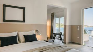 A hotel room with a large bed, a chair, a balcony with a view of the sea, and a framed picture on the wall.