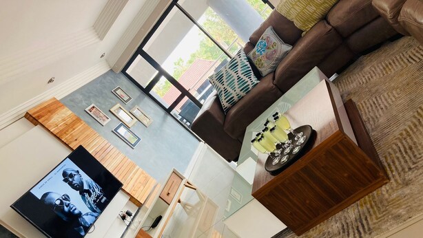 A modern living room with a large flat-screen TV, a brown leather sofa, a coffee table with drinks, and a patterned rug. - On Hill Lodge (Bloemfontein)