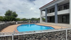 A swimming pool surrounded by a metal fence, with a reception area in the background. - On Hill Lodge (Bloemfontein)