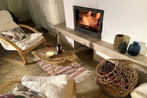 A cozy living room with a fireplace, a comfortable chair, a small table with a candle, and decorative items. - Holiday home in the countryside, with pool, garden (Rozewko)