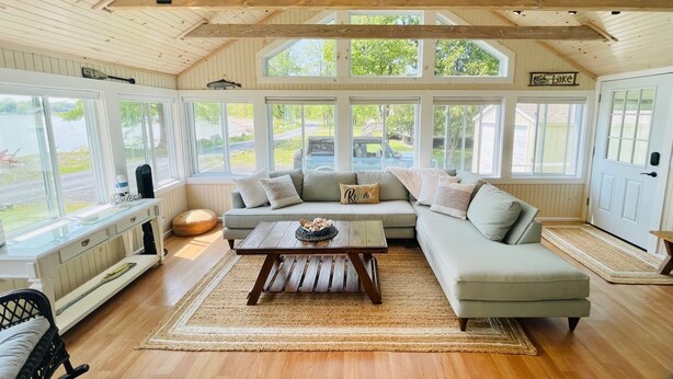 L’intérieur chaleureux d’un chalet avec un plafond en bois, de grandes fenêtres, un canapé d’angle et une table basse en bois.