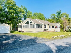 A single-story house with a large front porch, a garage, and a covered patio area. - Bright 3 Bedroom Lake Cottage with dock! (North Hero)