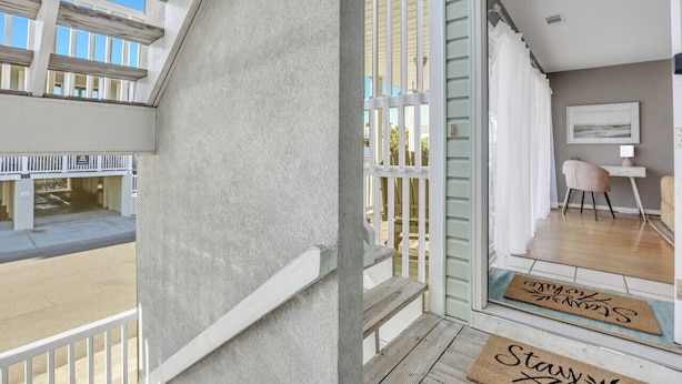 A balcony with a view of a building, a wooden deck, and a door with a mat that says "Stay".