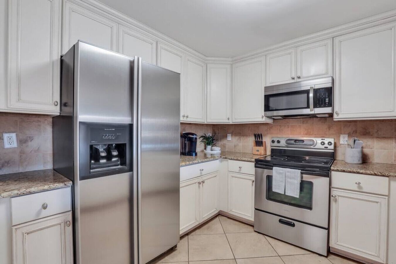 Una cocina con armarios blancos, un refrigerador de acero inoxidable, un microondas y una estufa.