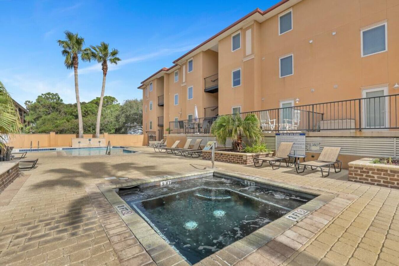 A hotel pool area with a hot tub, lounge chairs, and palm trees.