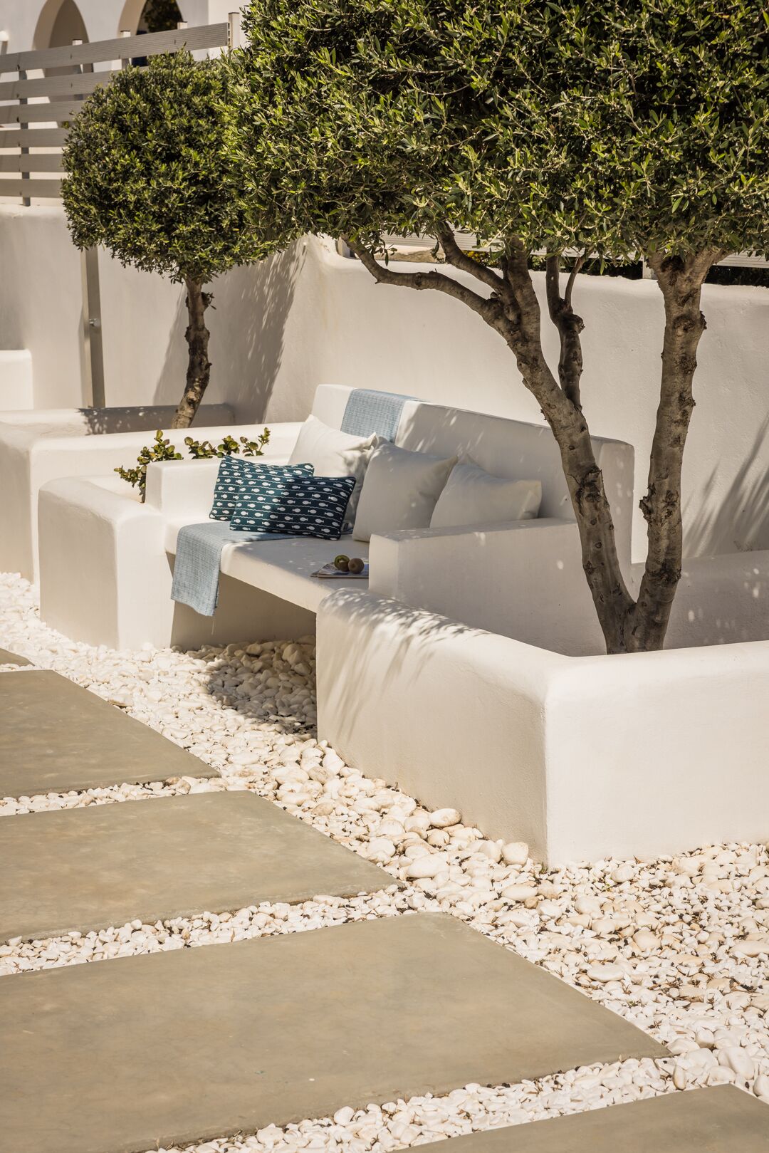A white outdoor seating area with a tree, white cushions, and a patterned pillow.