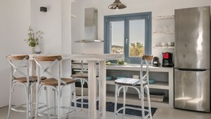 Eine moderne Küche mit weißen Schränken, einem Edelstahl-Kühlschrank, einem Esstisch mit vier Stühlen und einem Fenster mit Blick ins Grüne.