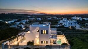 Eine moderne Villa mit Dachterrasse, Schwimmbad und Blick auf die umliegende Wohngegend bei Sonnenuntergang.