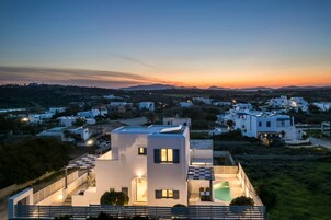 Uma villa moderna com terraço no telhado, piscina e vista para a área residencial ao redor durante o pôr do sol.