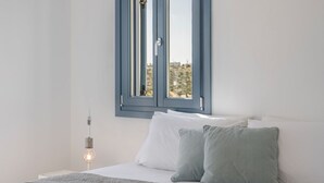 Ein Schlafzimmer mit Bett, Kissen, einer Nachttischlampe und einem Fenster mit Blick auf Gebäude.