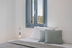 A bedroom with a bed, pillows, a bedside lamp, and a window with a view of buildings.