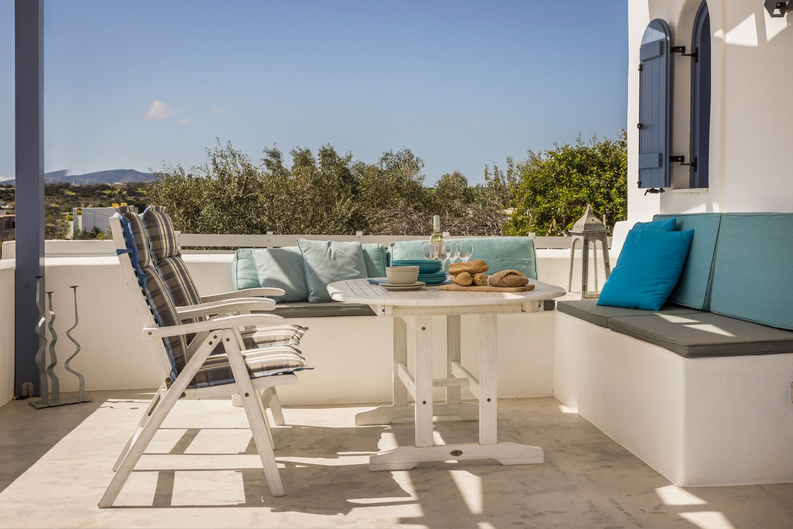 A terrace with a white table, a cushioned bench, and a view of the landscape.