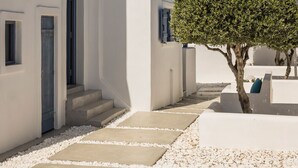 Ein weißes Gebäude mit einer Treppe, die zu einer Tür führt, ein Baum im Vordergrund und ein klarer, blauer Himmel.