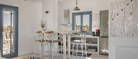 Una cocina moderna con armarios blancos, una zona de comedor con taburetes de bar y un amplio ventanal con vistas al exterior.