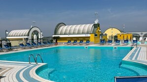 A swimming pool with blue water, surrounded by lounge chairs and a tiled deck. - App.Mare V&V res.Colombo with swimmingpool+solarium News - Caorle, Veneto, Italy (Caorle)