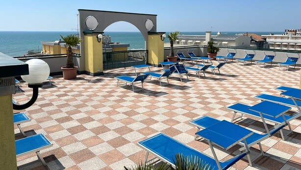 A rooftop terrace with blue lounge chairs, a checkered floor, and a view of the sea. - App.Mare V&V res.Colombo with swimmingpool+solarium News - Caorle, Veneto, Italy (Caorle)