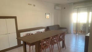 A dining area with a wooden table and chairs, a sofa, and a sliding glass door leading to an outdoor area. - App.Mare V&V res.Colombo with swimmingpool+solarium News - Caorle, Veneto, Italy (Caorle)