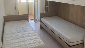A bedroom with two single beds, a wardrobe, and a sliding glass door leading to a balcony. - App.Mare V&V res.Colombo with swimmingpool+solarium News - Caorle, Veneto, Italy (Caorle)