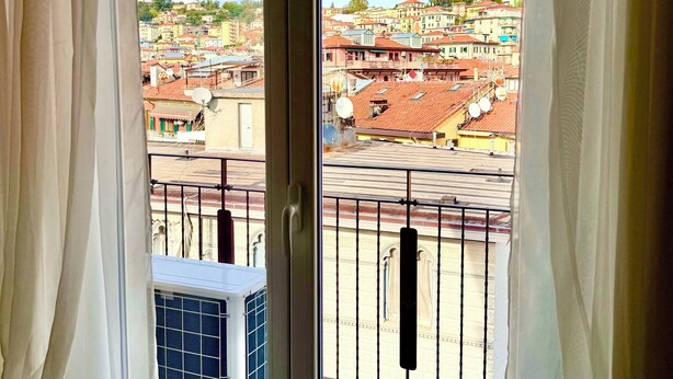 Vista desde una ventana con cortinas blancas, con vistas a un paisaje urbano con edificios y cielo despejado.