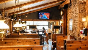 Un interior rústico con bancos y mesas de madera, una pantalla de televisión y una pared de piedra.
