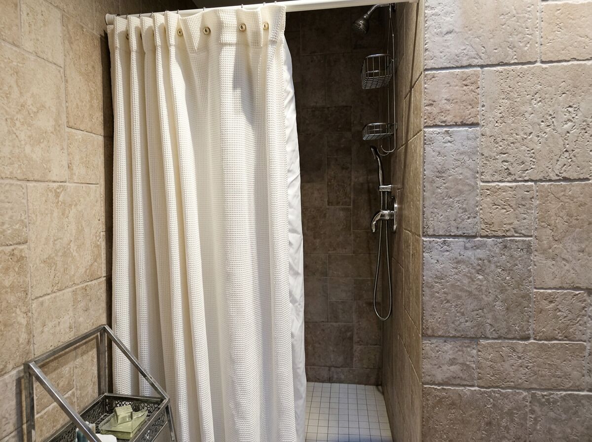 A shower with a curtain, a metal shower head, and a tiled floor.
