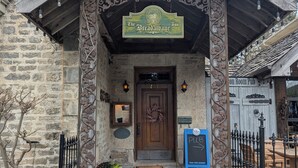 A stone building with a wooden entrance, a sign reading 'The Breadalbane Inn,' and a door with a wreath. There are potted plants and a chalkboard sign outside.