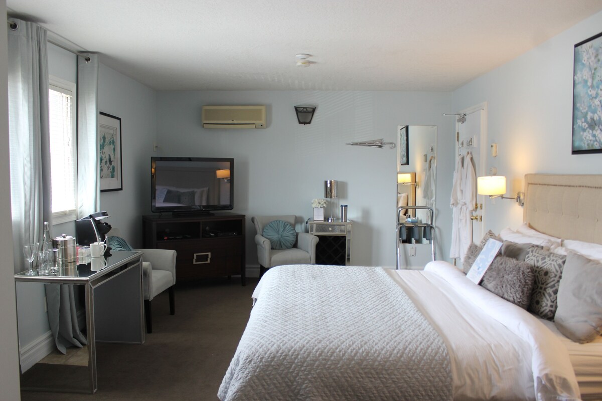 A hotel room with a bed, a desk, a chair, a TV, and a bathroom.