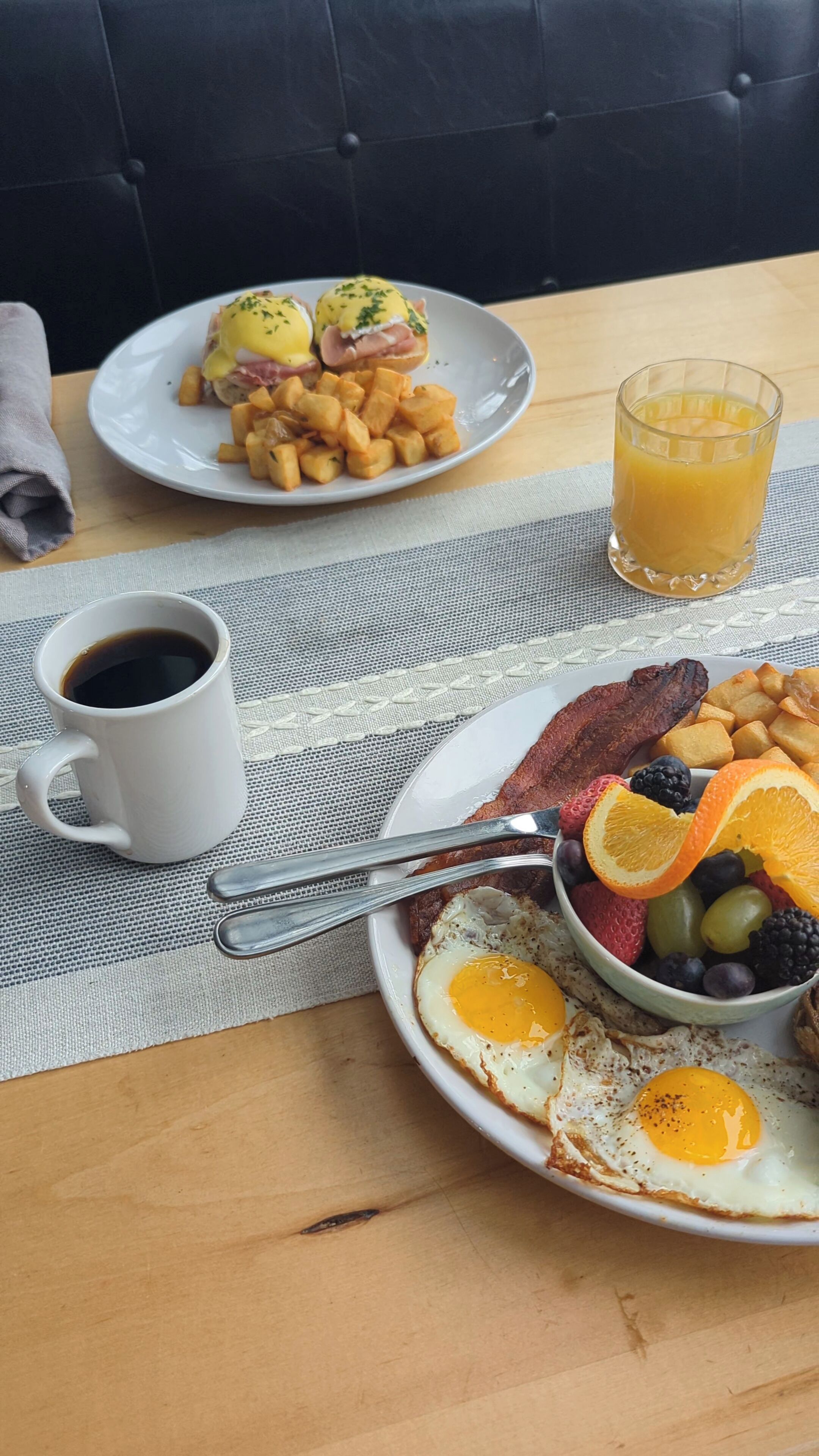 A breakfast setting with eggs, bacon, toast, and fruit on a table.