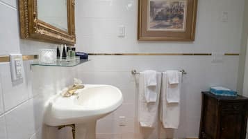 Un baño con lavamanos blanco, espejo con marco dorado, cuadro enmarcado y suelo de madera.