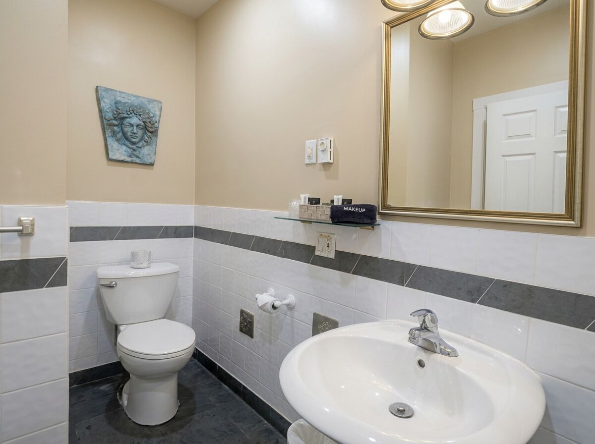 Une salle de bain comprenant des toilettes, un lavabo, un miroir et un élément décoratif mural.