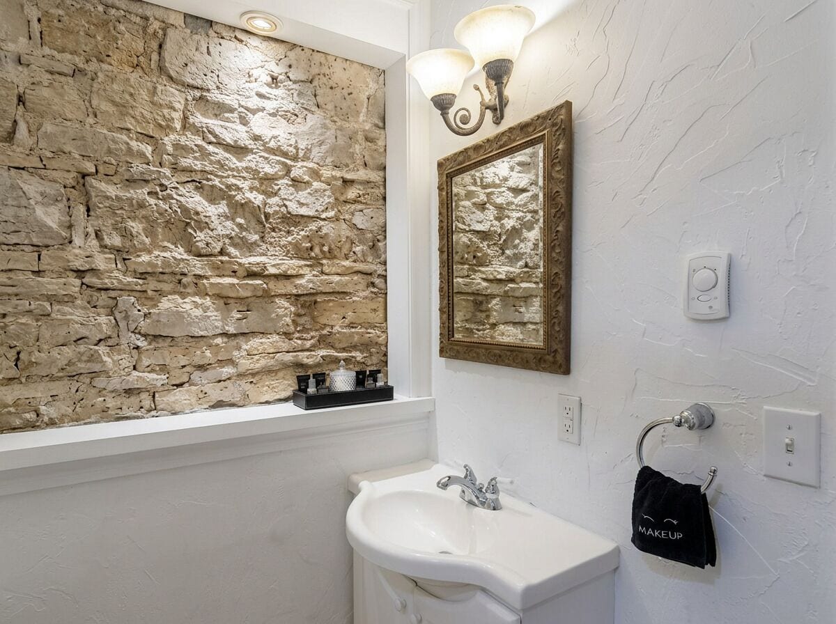 A bathroom with a stone wall, a white sink, a mirror, and a towel rack.