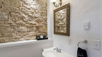 A bathroom with a stone wall, a white sink, a mirror, and a towel rack.