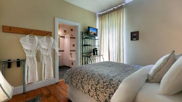 A bedroom with a bed, a mirror, a door leading to a bathroom, and a TV on a stand.