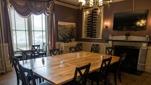 A dining room with a large wooden table, dark wooden chairs, a fireplace, a mounted wine rack, and a television on the wall.
