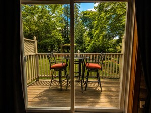 A deck with a table and chairs, a wooden railing, and a view of trees.